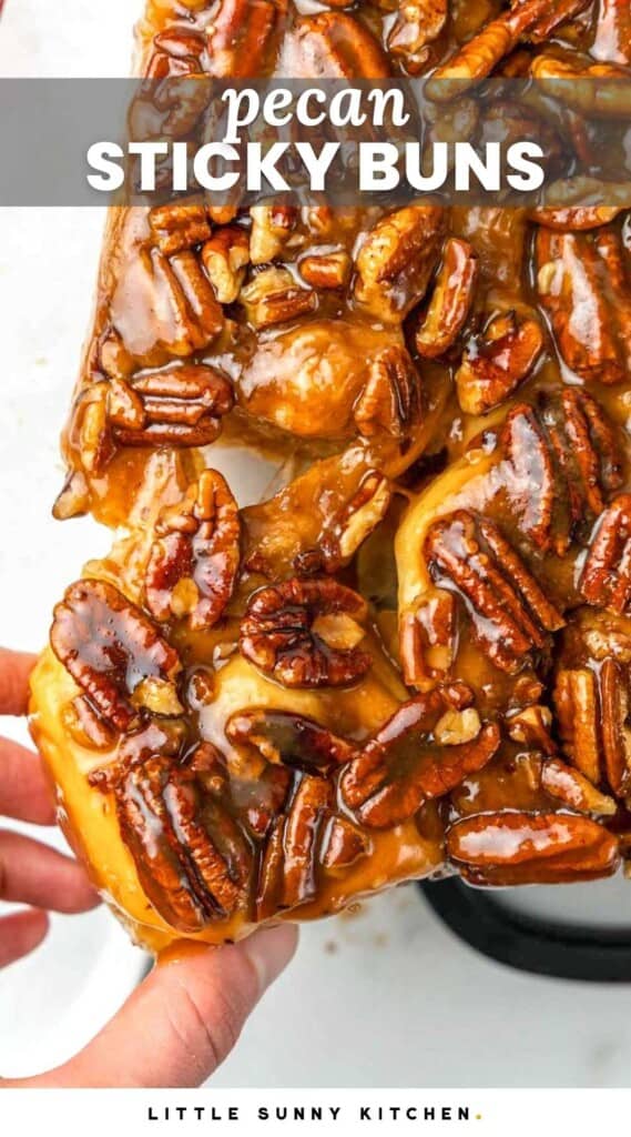a hand pulling a pecan sticky bun away from the rest.