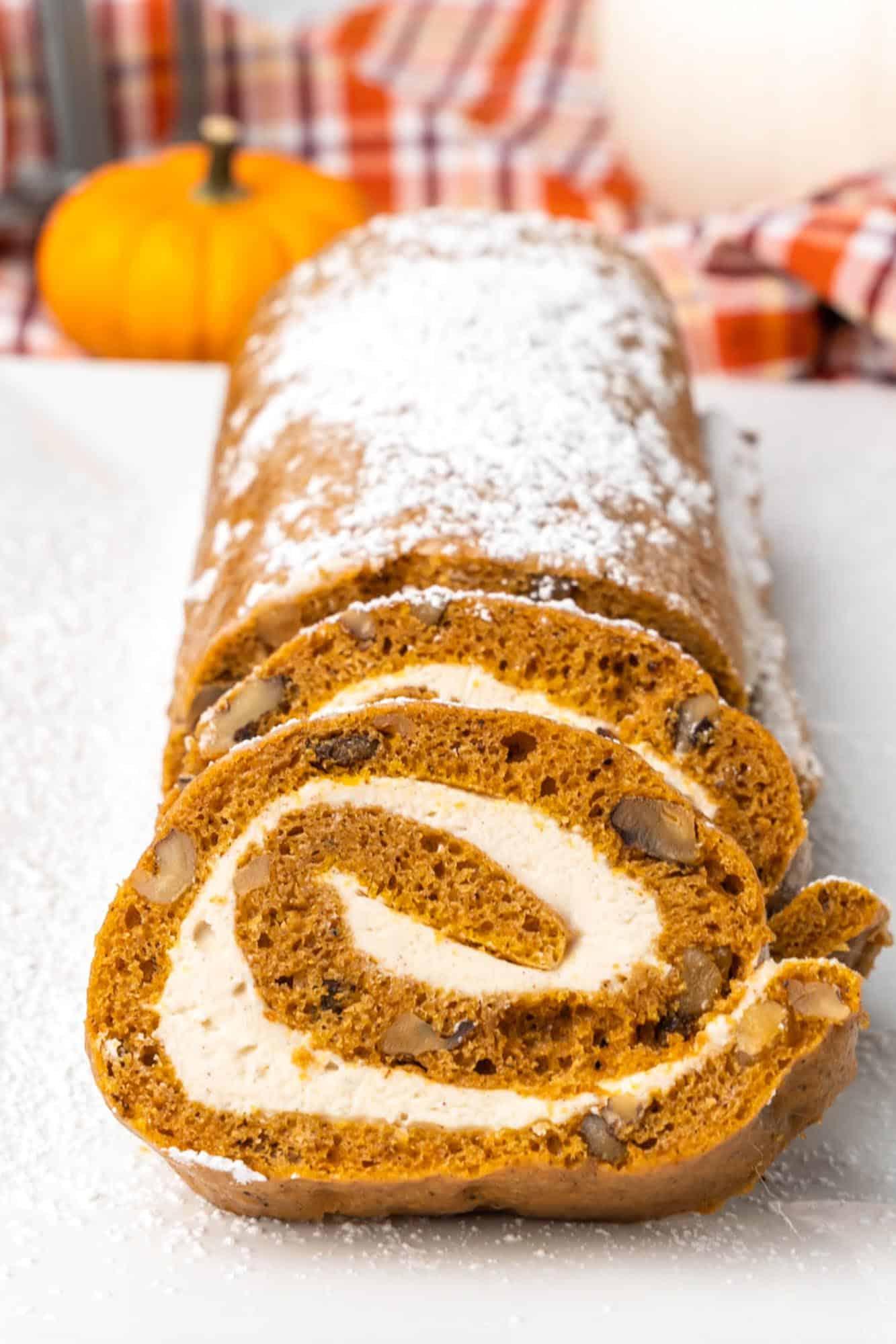 Sliced pumpkin roll cake, viewed from one end. Slices show cream cheese frosting swirled inside.