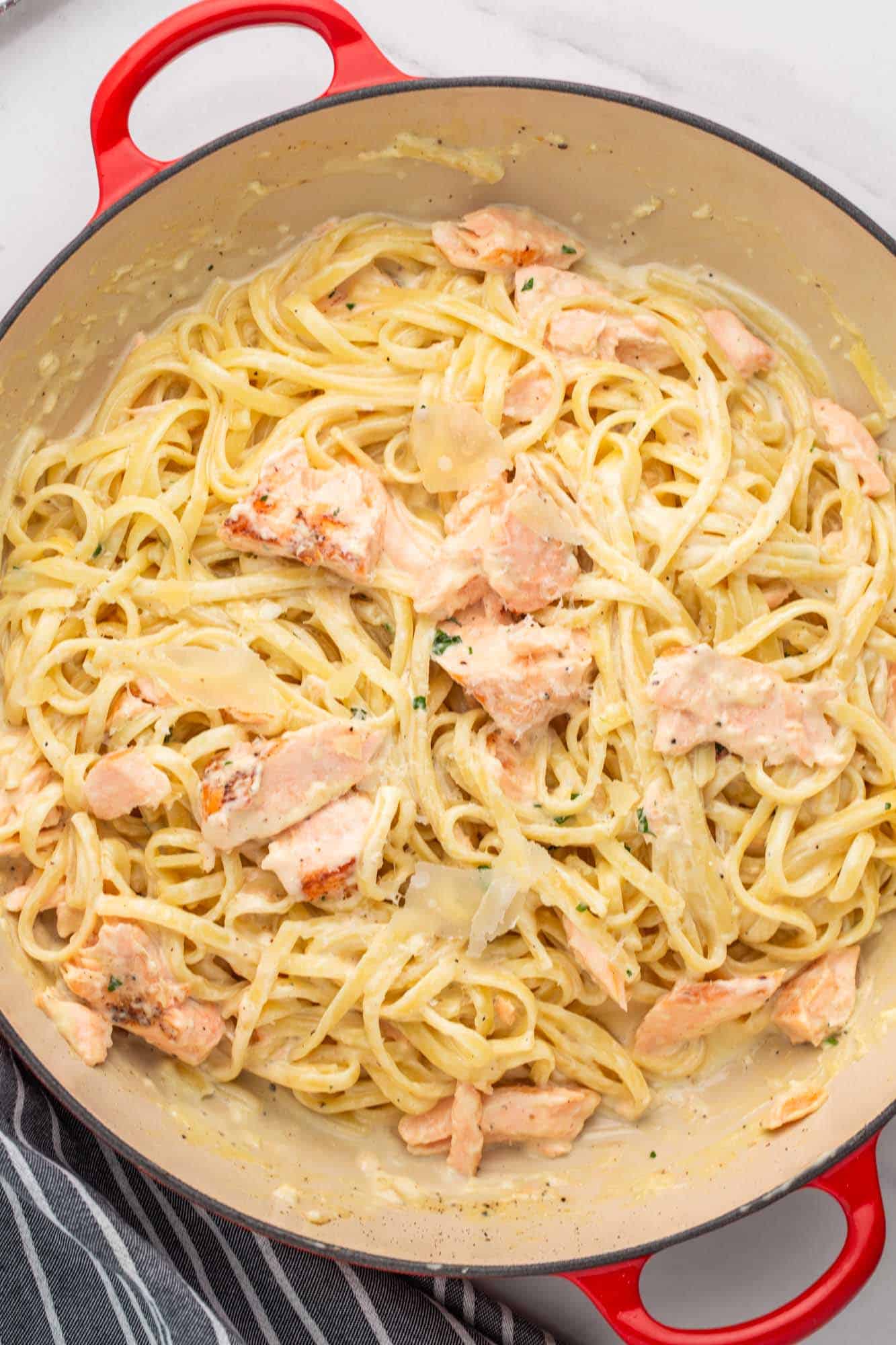 a large, enameled, two-handled skillet filled with salmon pasta in cream sauce