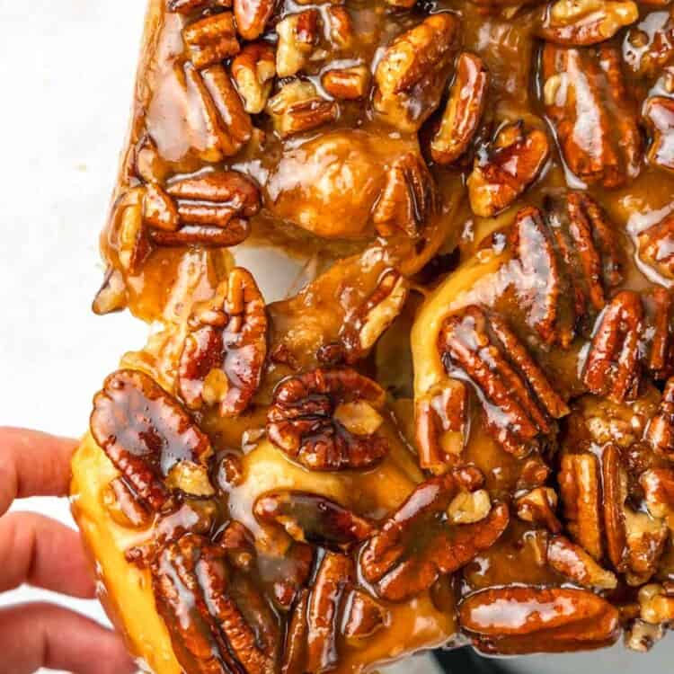 a hand pulling a pecan sticky bun away from the rest.