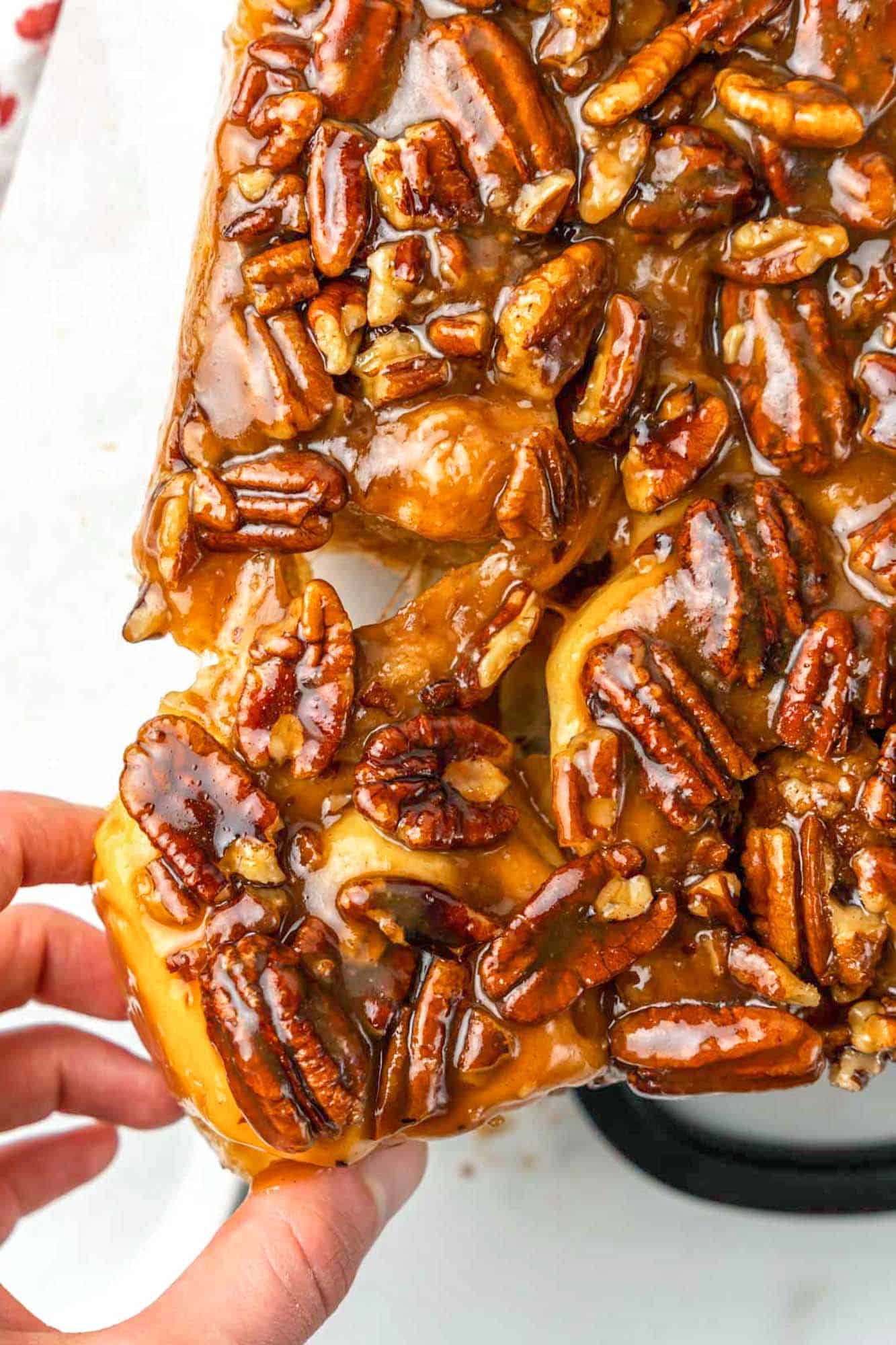 a hand pulling a pecan sticky bun away from the rest. 