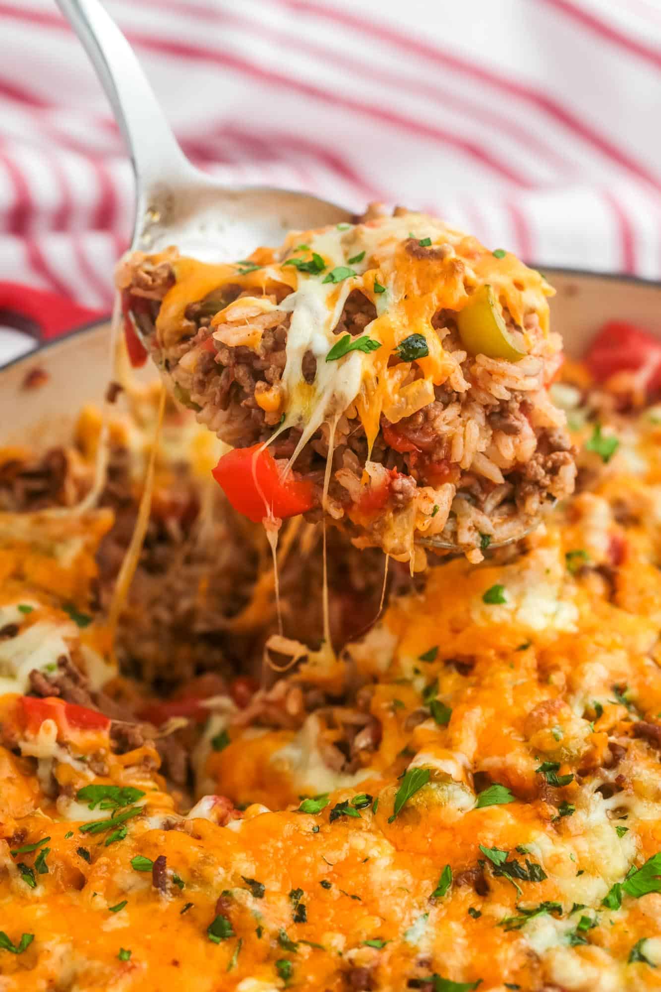 stuffed pepper casserole in a skillet. A spoon is lifting up a serving showing melty cheese. 