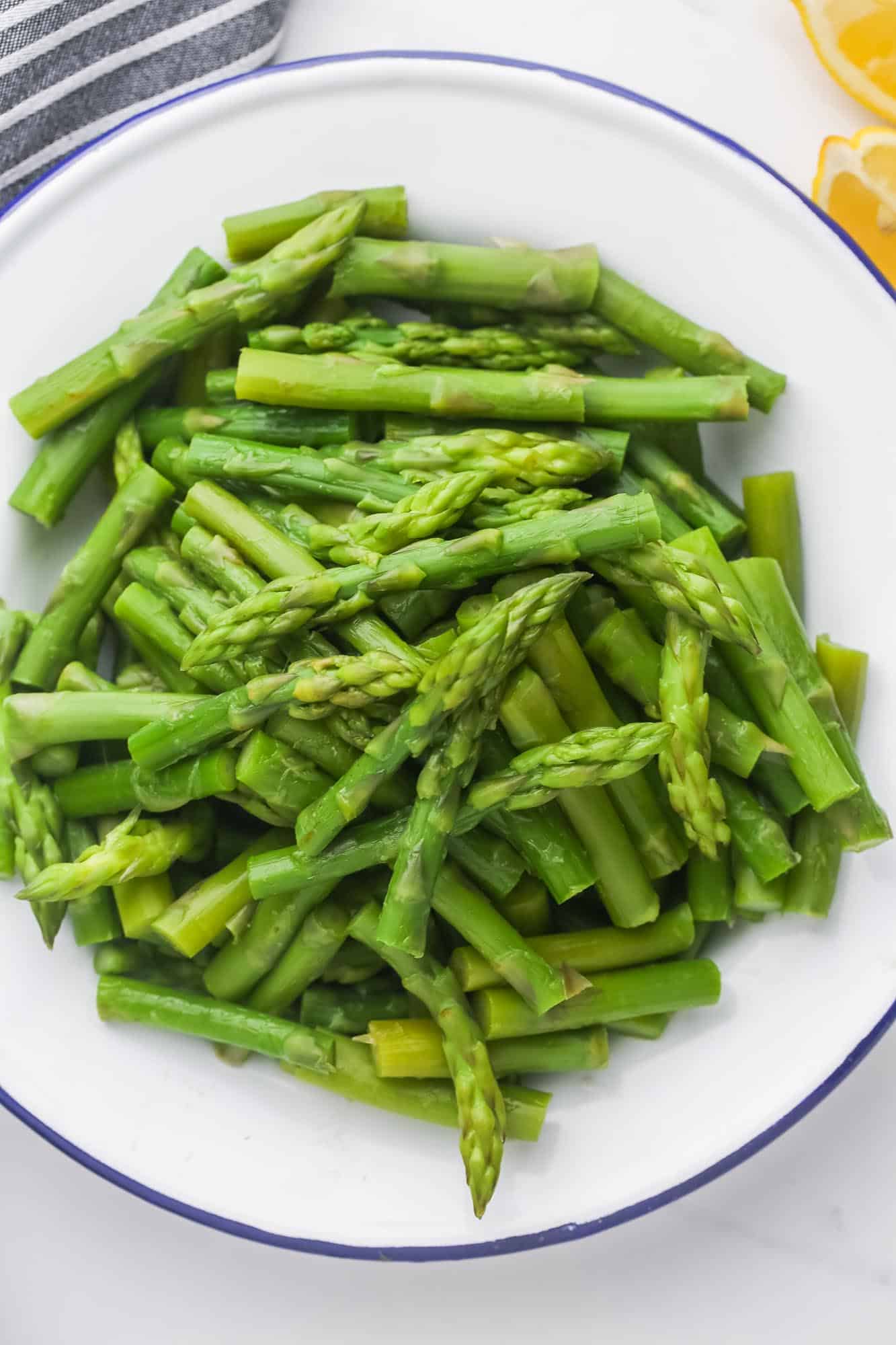 Blanched asparagus spears that are cut into 2-inch pieces, on a white plate.