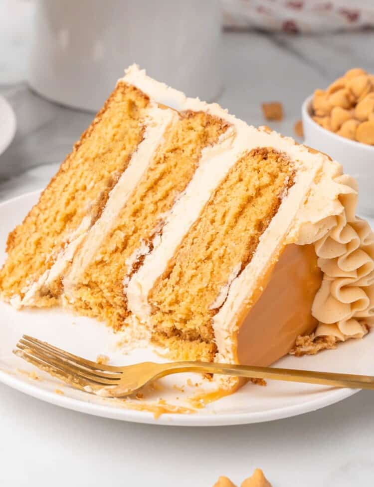 a large wedge slice of a three layer butterscotch cake, on its side on a plate. A fork is on the plate.