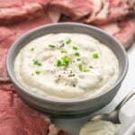 Horseradish sauce in a small gray bowl, and slices of prime rib on the sides of the sauce