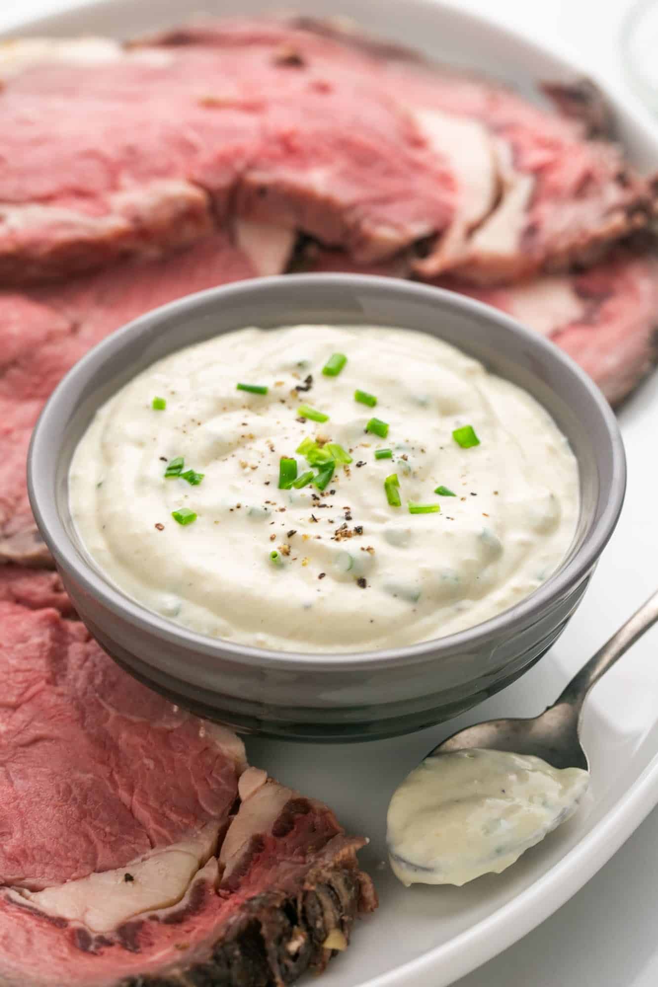 Horseradish sauce in a small gray bowl, and slices of prime rib on the sides of the sauce