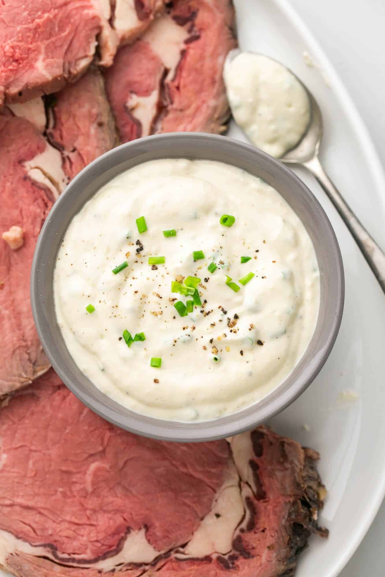 Overhead shot of horseradish sauce in a bowl, with prime rib slices on the side.
