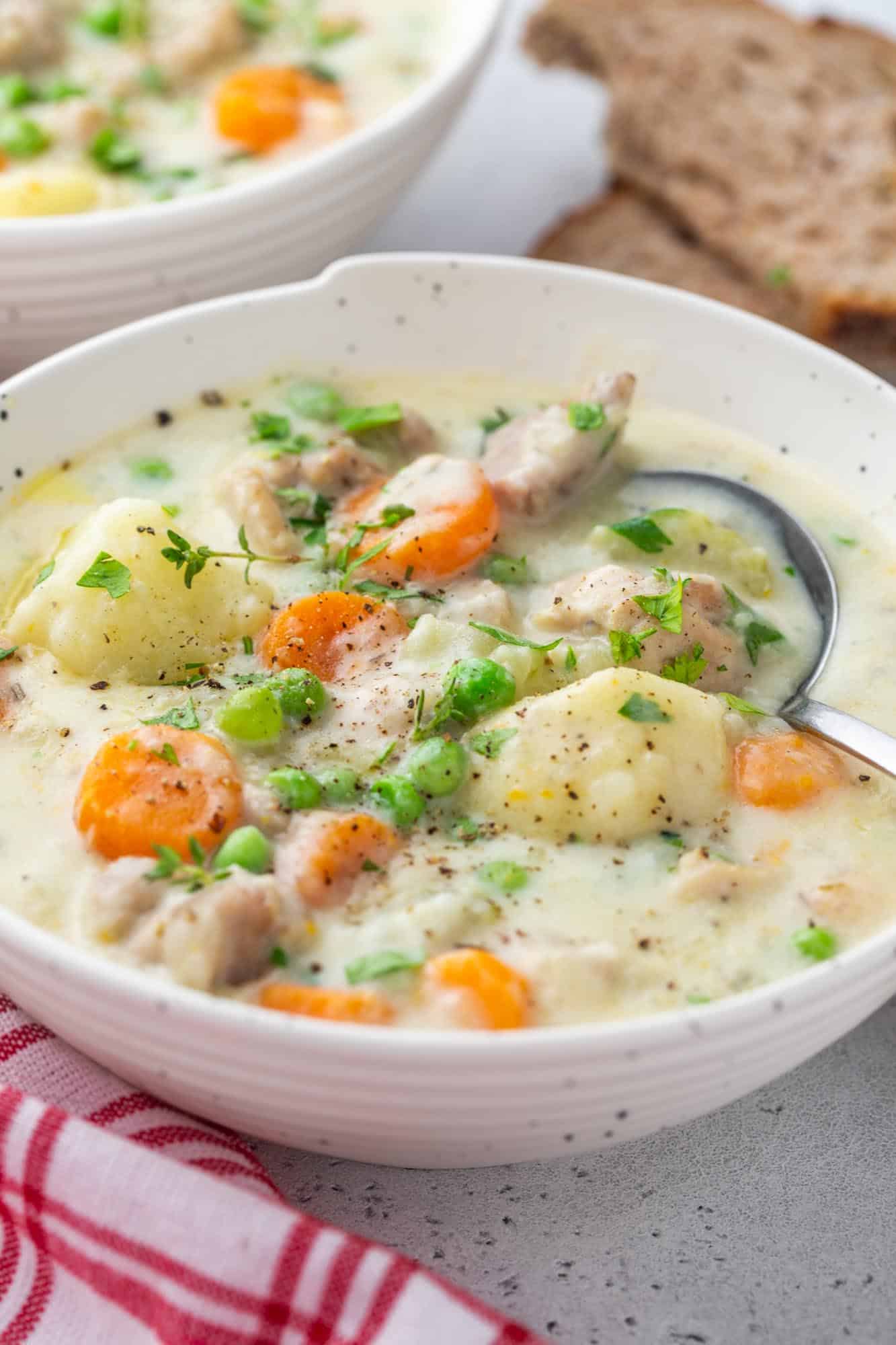 a white bowl filled with creamy chicken stew with peas and carrots.