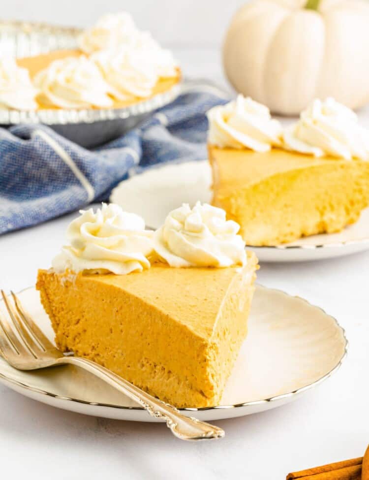 a slice of creamy no bake pumpkin pie topped with whipped cream rosettes, on a dessert plate with a fork.