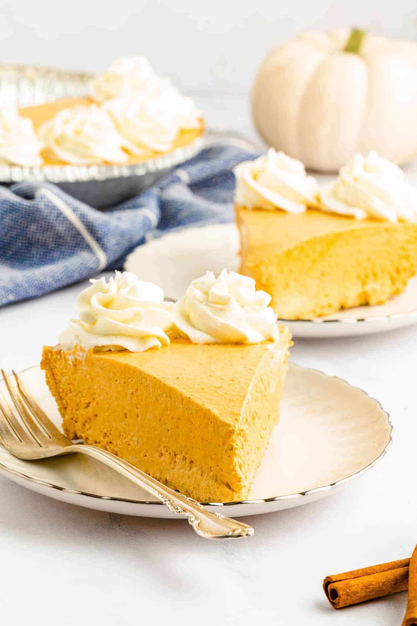 a slice of creamy no bake pumpkin pie topped with whipped cream rosettes, on a dessert plate with a fork.