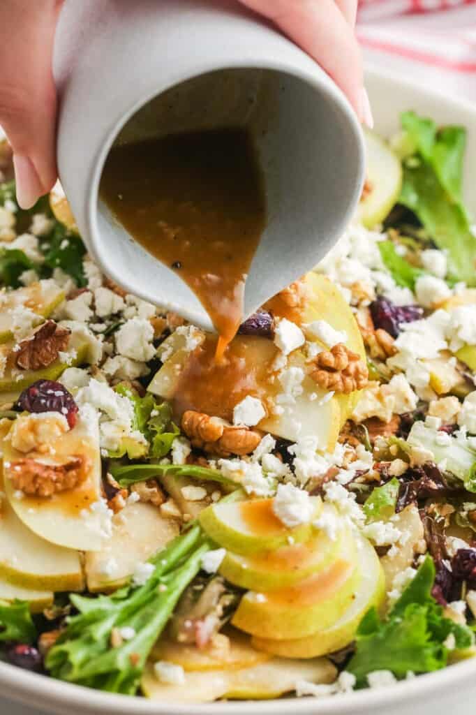 a hand pouring balsamic dressing on a pear feta salad