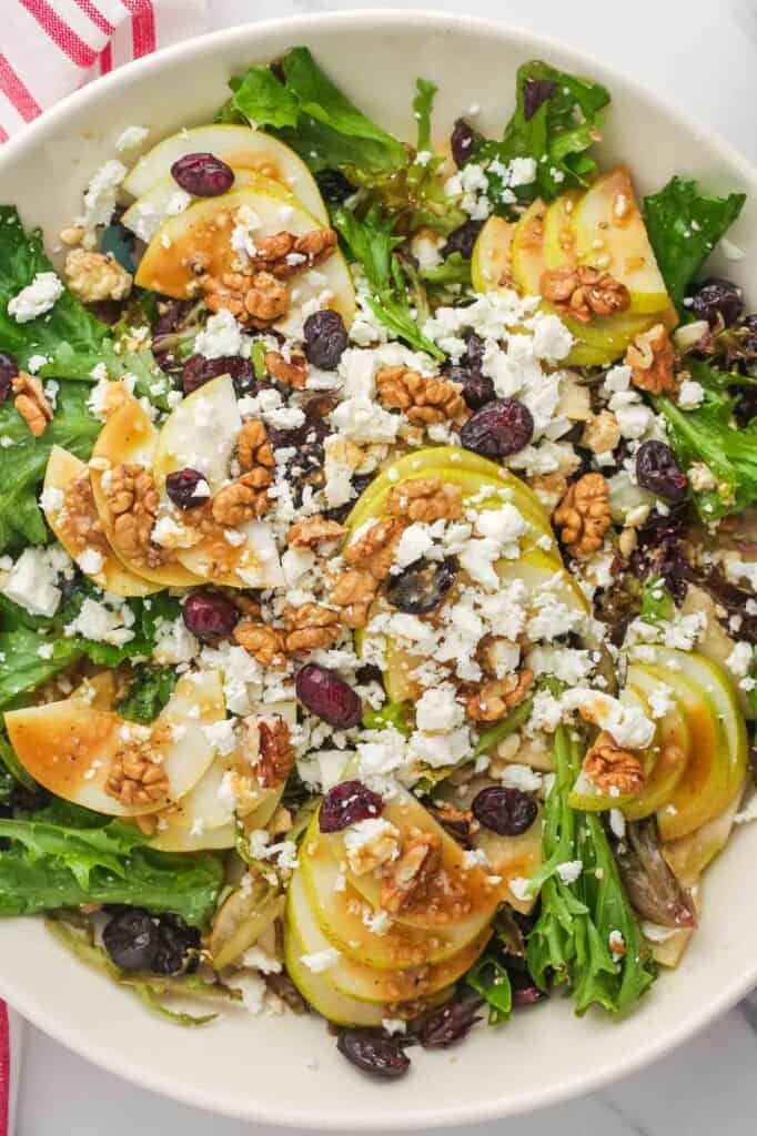 a large salad bowl filled with mixed greens topped with sliced pears, walnuts, feta, and dressing.