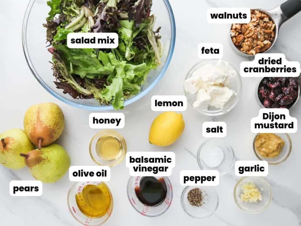 The ingredients in a fall pear salad, all in small bowls on the counter. Text overlay labels each ingredient.