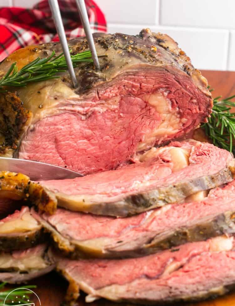 A sliced prime rib roast on a cutting board. A two-tined fork is holding the roast.