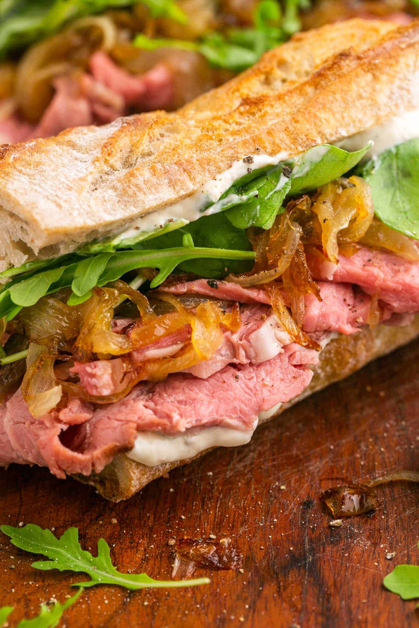 closeup view of a prime rib sandwich with rare beef, creamy horseradish sauce, caramelized onions, baby arugula, all layered on a split baguette.