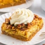 A slice of pumpkin dump cake served on a small white plate, topped with fresh whipped cream
