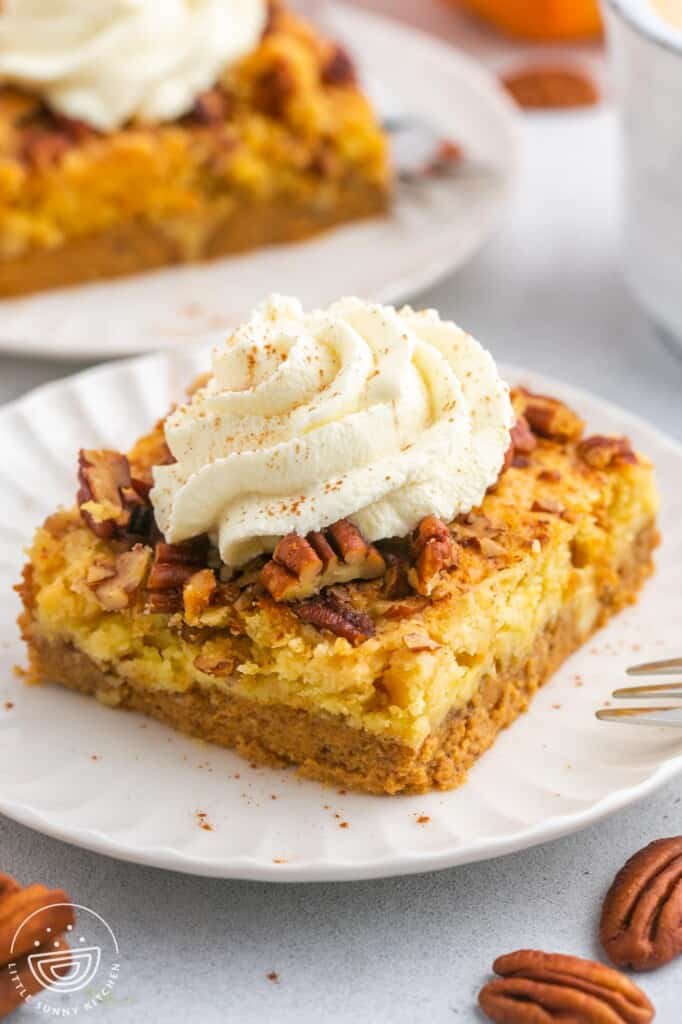 A slice of pumpkin dump cake served on a small white plate, topped with fresh whipped cream