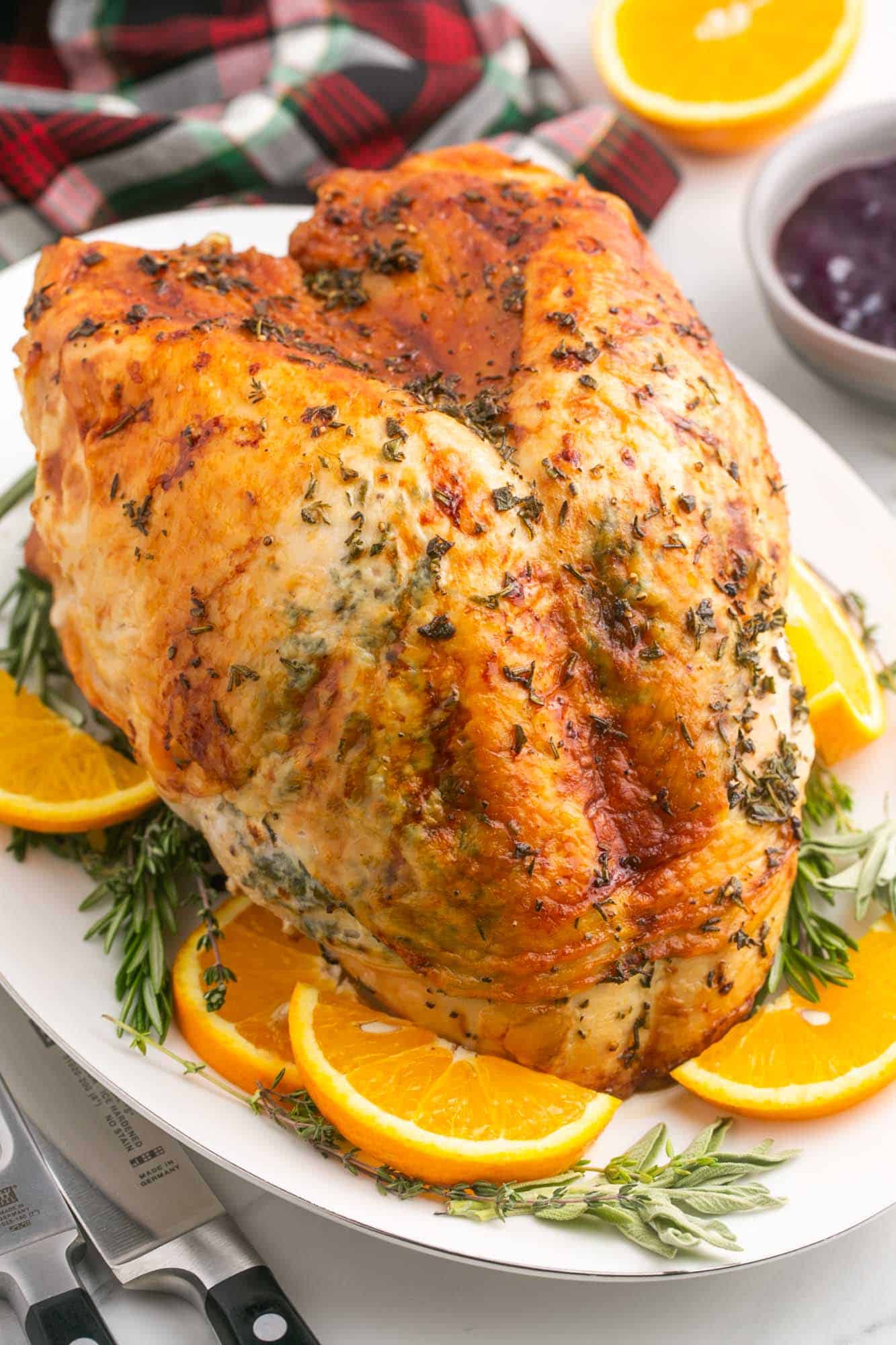 a browned roasted turkey breast on a white platter surrounded by orange slices and herbs.