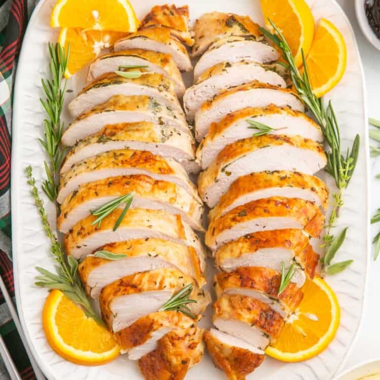 turkey breast meat sliced and arranged in two rows on a white platter surrounded by orange slices