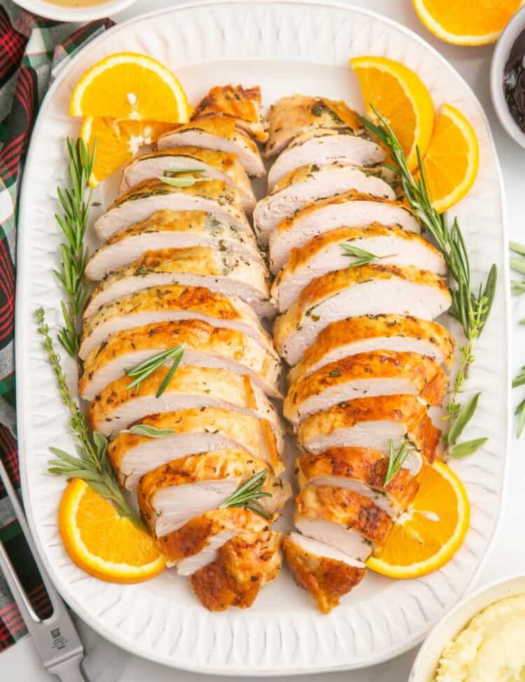 turkey breast meat sliced and arranged in two rows on a white platter surrounded by orange slices