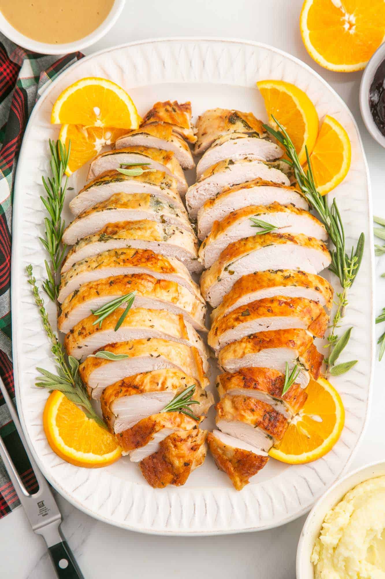 turkey breast meat sliced and arranged in two rows on a white platter surrounded by orange slices