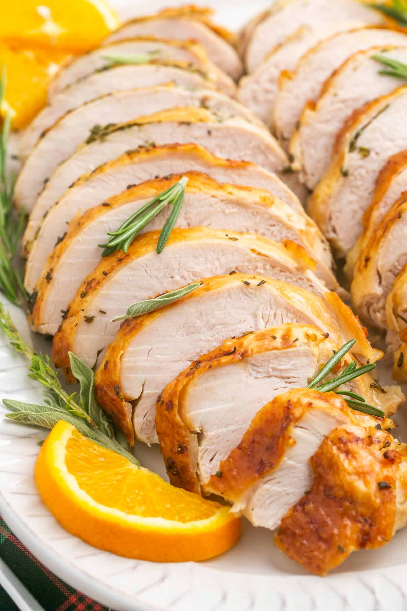 close up view of sliced roast turkey breast with crispy skin, garnished with fresh herbs and oranges.