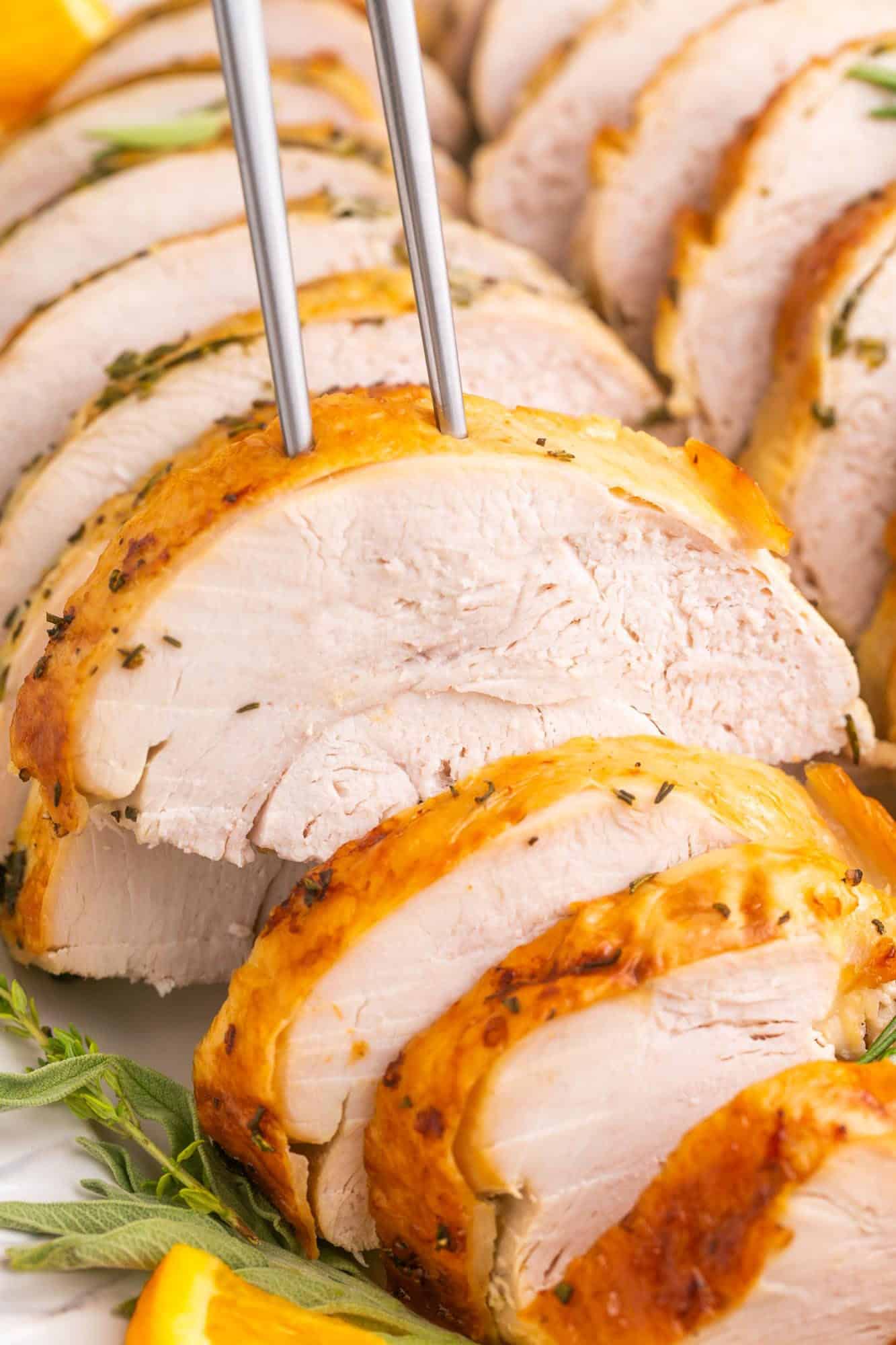 close up view of sliced roast turkey breast with crispy skin, a two pronged fork is picking up a piece.