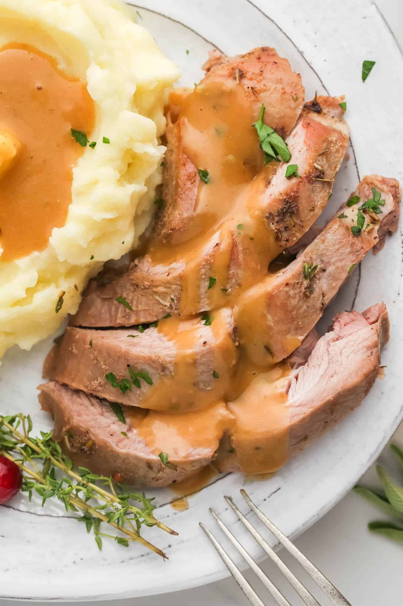 Sliced dark meat turkey on a plate, topped with gravy, next to a serving of mashed potatoes with gravy.