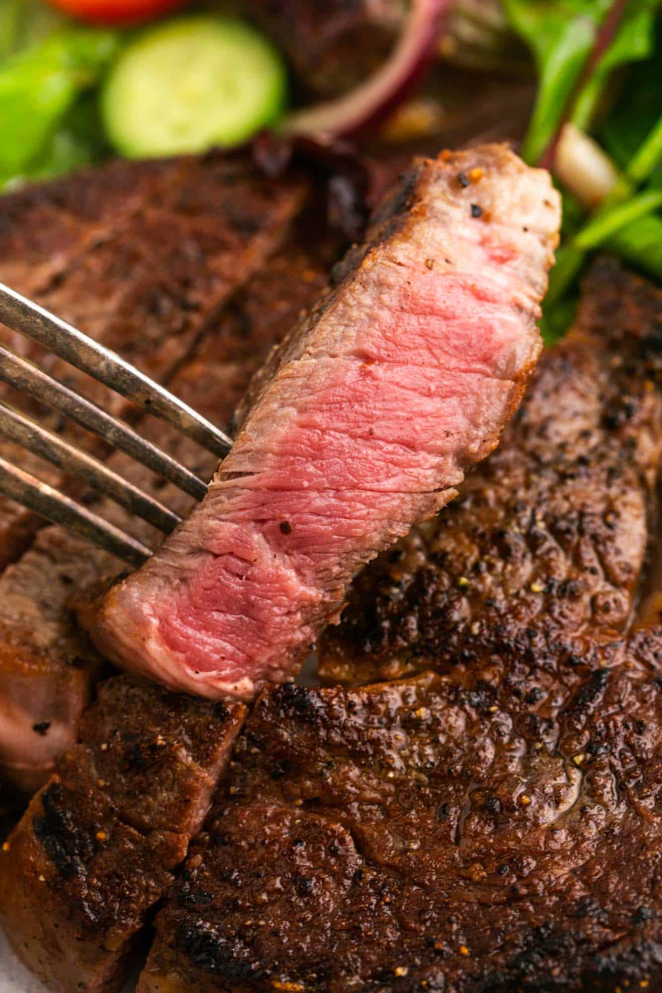 medium rare steak held by a fork over a seared steak.