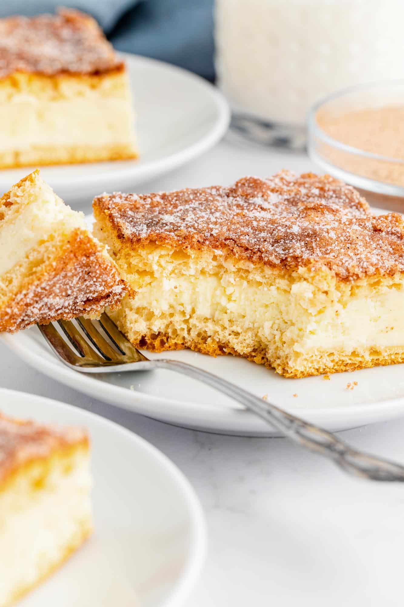 A square piece of sopapilla cheesecake on a plate. a fork has removed a pice from the front corner.