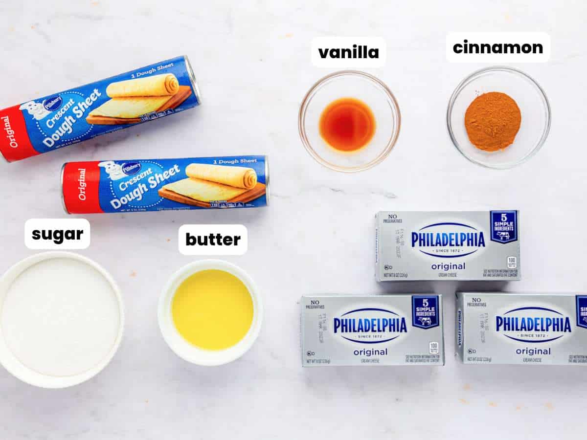 two rolls of crescent roll dough, three blocks of cream cheese, and the ingredients needed to make sopapilla cheesecake in small bowls. Each ingredient is labeled with a text box overlay.