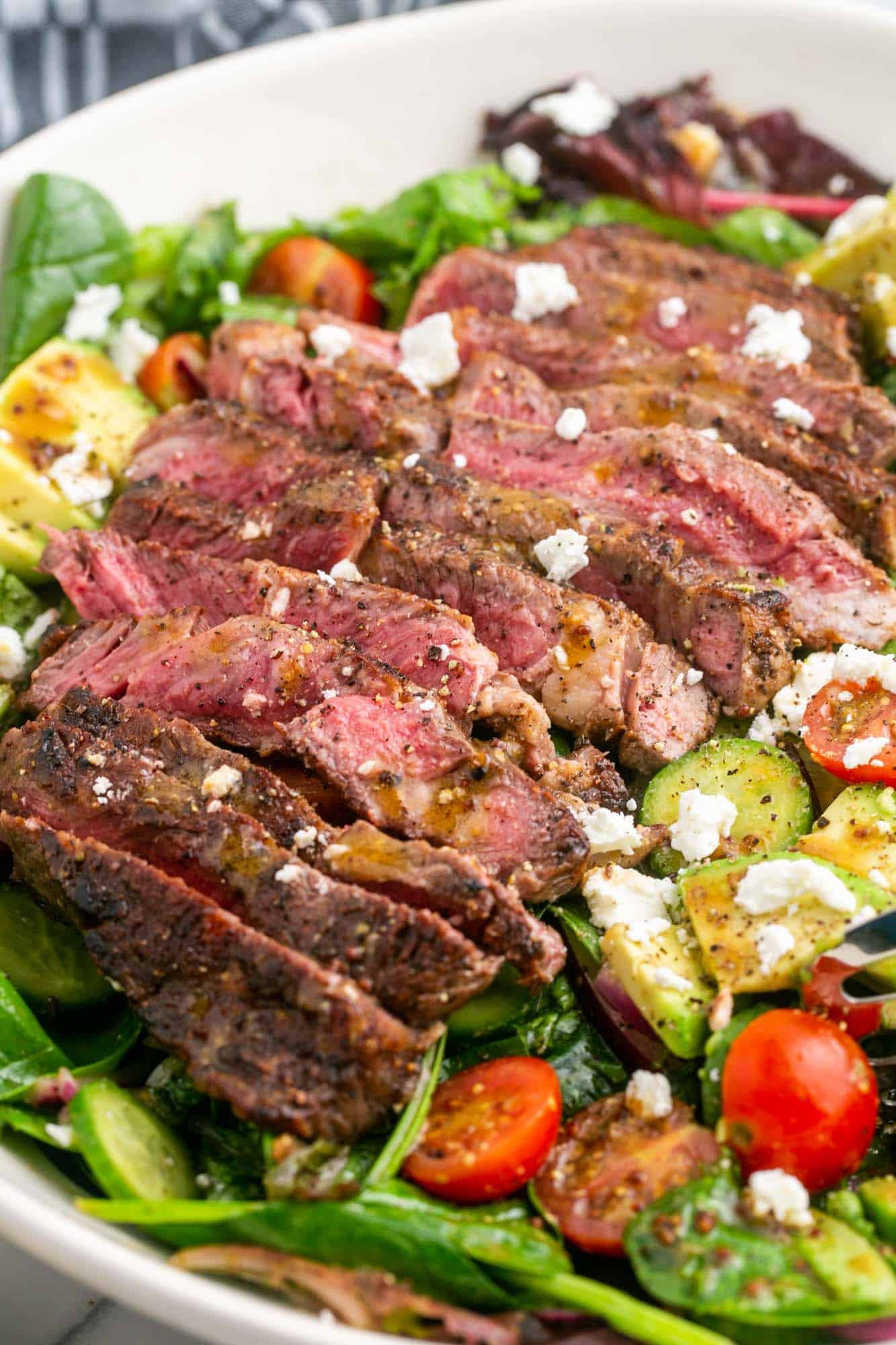 closeup shot of a sliced steak on top of a salad, drizzled with dressing and topped with crumbled feta
