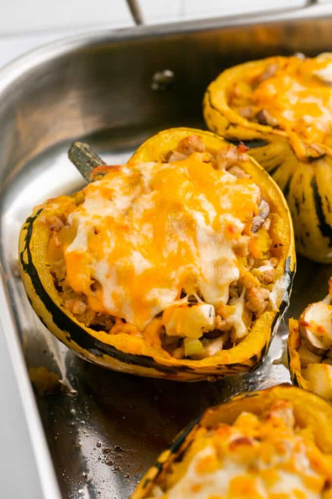 Cheesy stuffed acorn squash half in a metallic roaster