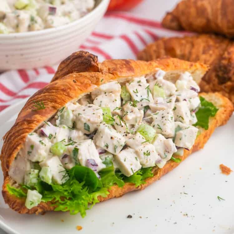 Butter croissant stuffed with turkey salad, placed on a white plate.