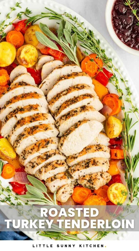 Overhead shot of sliced turkey tenderloin in a large oval white platter, with roasted vegetables and fresh herbs. And overlay text that says "roasted turkey tenderloin"