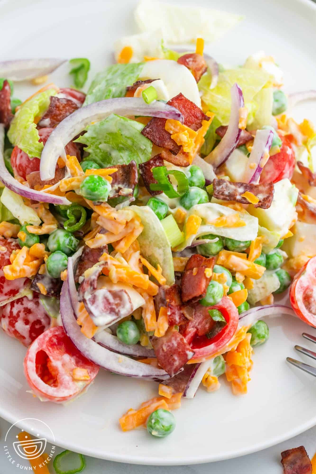A dinner plate with 7 layer salad with a creamy dressing. The salad includes cherry tomatoes, bacon, eggs, red onion, peas, and bacon