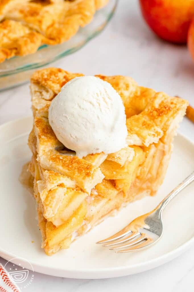 a large slice of apple pie with a lattice top. there's a scoop of ice cream on top of the pie, which is on a plate. there's a fork on the plate.