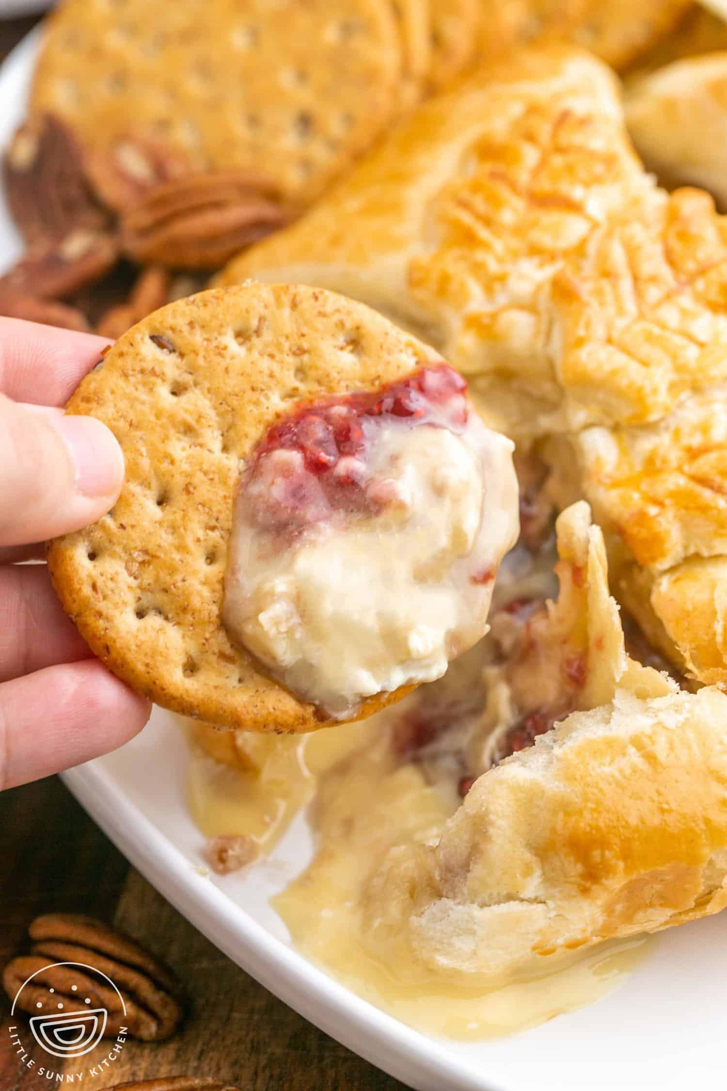 Melty brie cheese on a cracker with raspberry jam