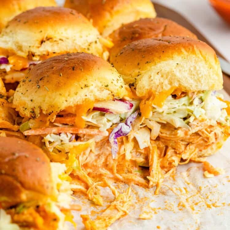 A pan of sliders with buffalo style shredded chicken, and coleslaw on them. sandwiches have been removed from the pan.