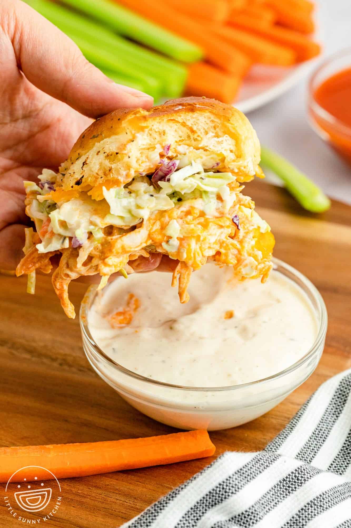 A hand is holding a buffalo chicken slider, dipping it into ranch dressing.