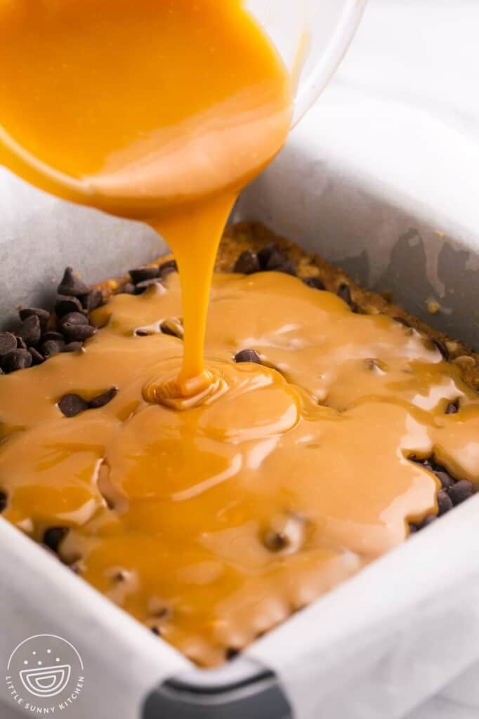 melted caramel being poured over chocolate chips on carmelitas bars