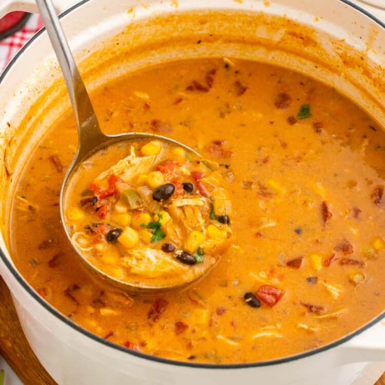 a white dutch oven of creamy chicken enchilada soup. a ladle is lifting soup out of the pot