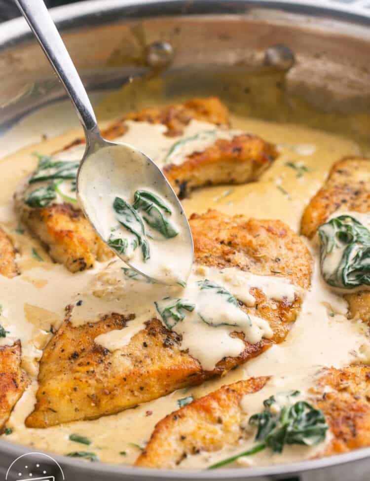 A spoon adding sauce to a chicken florentine cutlet in a pan with spinach.