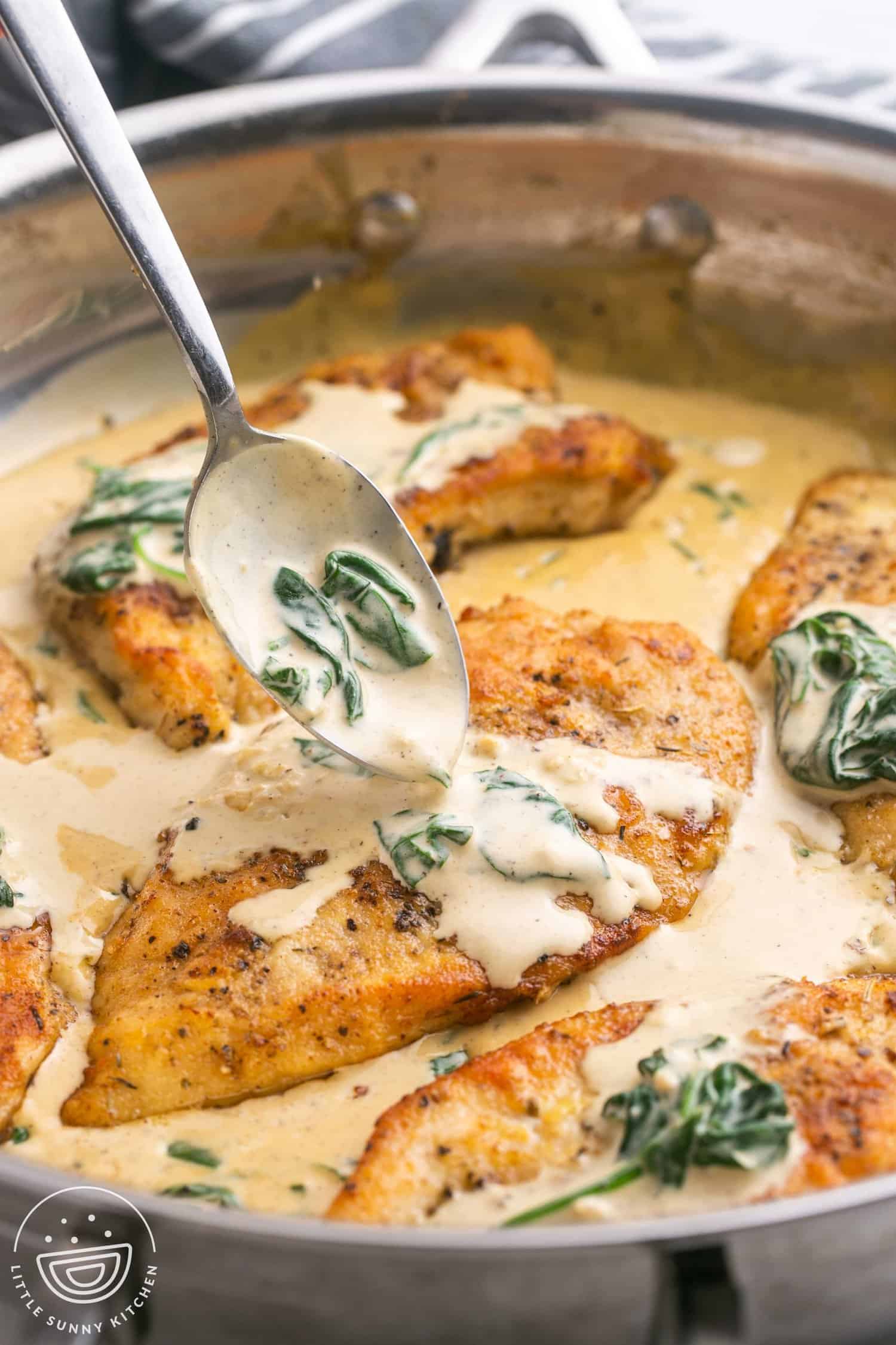 A spoon adding sauce to a chicken florentine cutlet in a pan with spinach. 