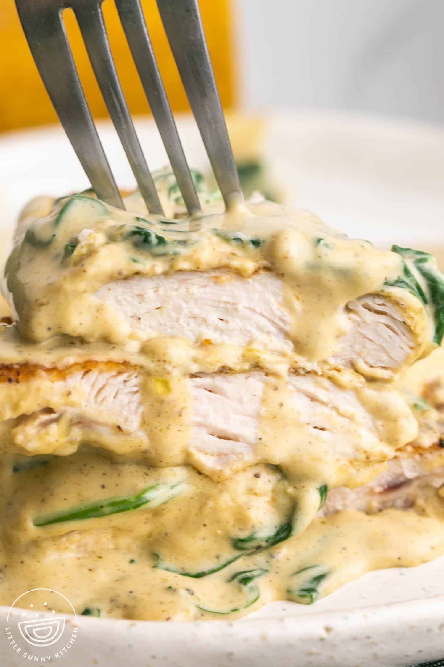 Slices of chicken florentine stacked on top of each other. A fork is holding them to show the texture of the chicken and creamy sauce. 