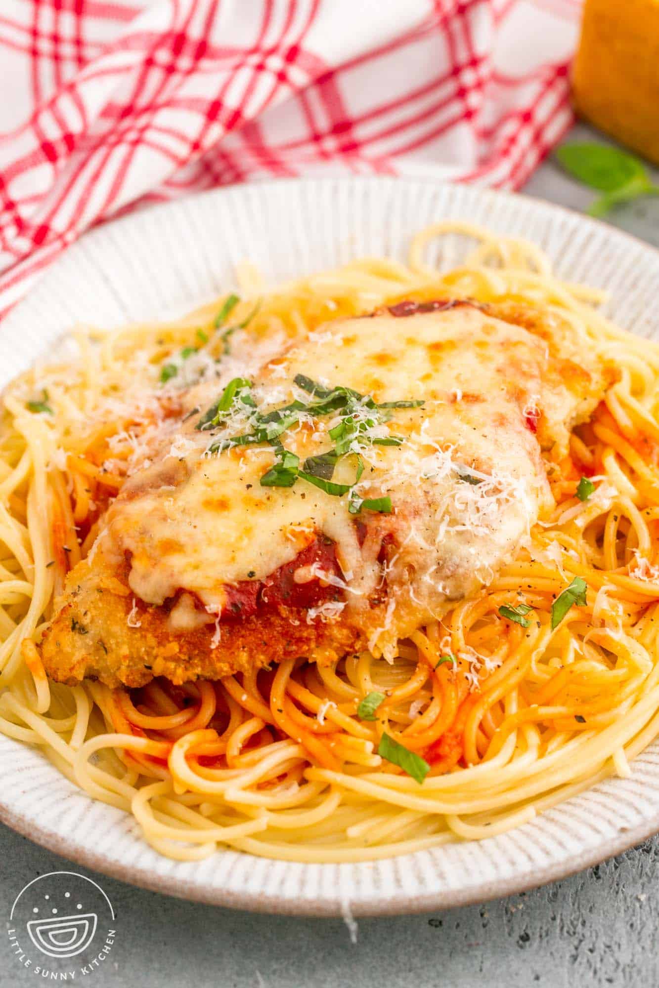 A chicken parmesan cutlet on top of spaghetti, on a white plate.
