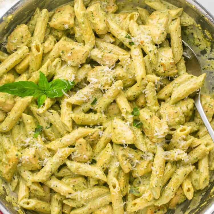 A two handled skillet filled with creamy pesto penne with chicken. A sprig of basil is added for garnish.