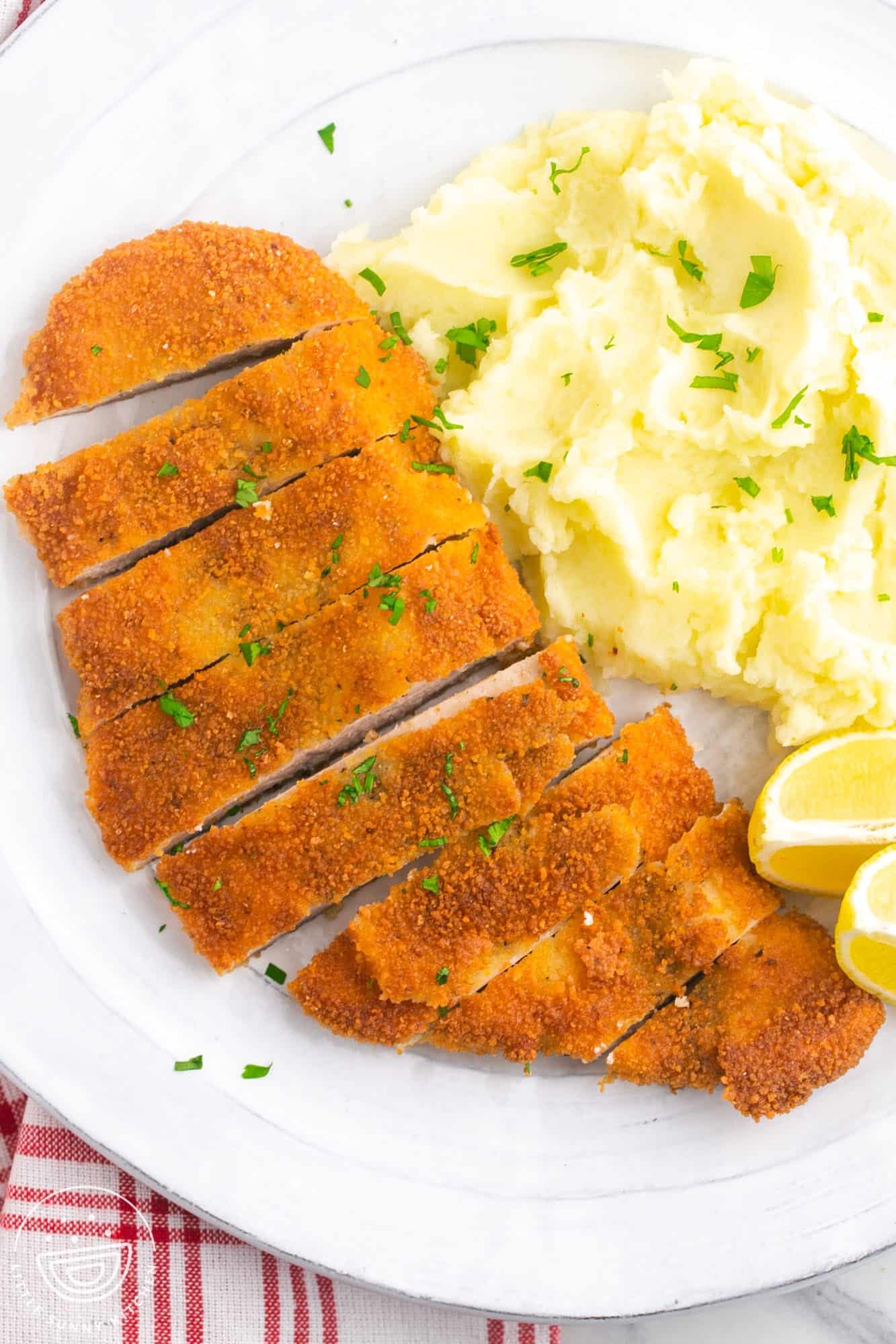 Sliced chicken schnitzel served with creamy mashed potatoes on a white plate