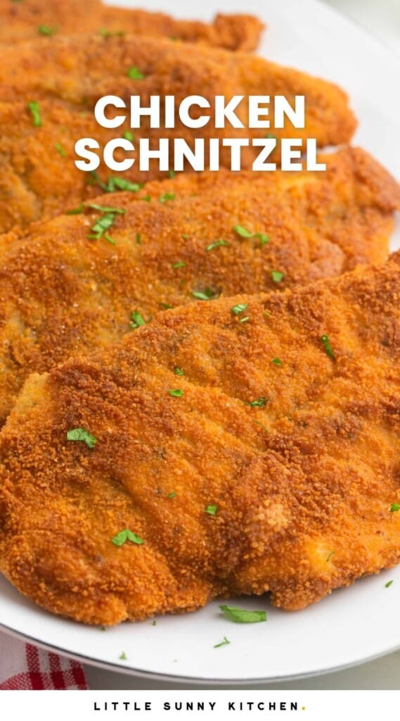 Breaded and fried chicken schnitzel cutlets served on a white platter, with overlay text that says "Chicken Schnitzel"