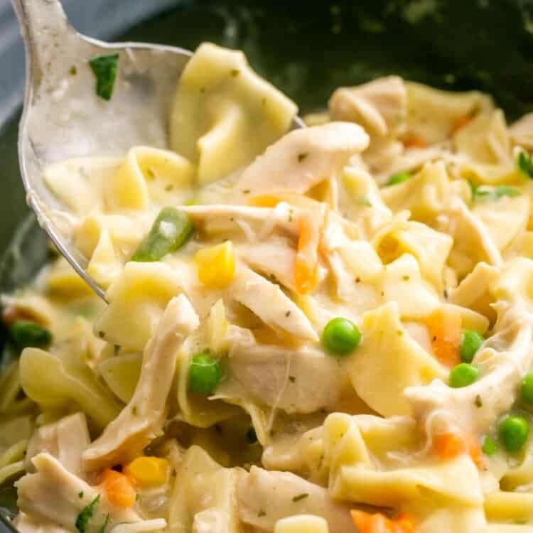 creamy chicken and noodles in a crockpot. A metal spoon is lifting some up to serve.